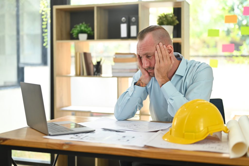photo of home builder seated at a desk looking frustrated du to delays in the schedule